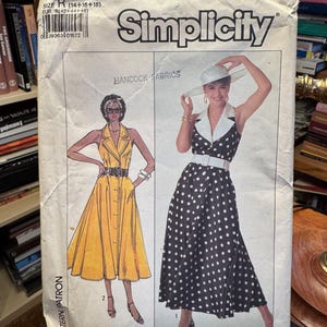 Könnte beinhalten: Ein Simplicity Schnittmusterumschlag 8061, Größe R (14+16+18). Die Vorderseite zeigt Illustrationen von zwei ärmellosen Kleidern mit breiten Reverskragen und Gürteln. Ein Kleid ist einfarbig gelb, das andere schwarz mit weißen Punkten.
