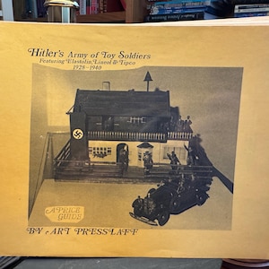 May include: A spiral-bound book with a tan cover titled Hitler's Army of Toy Soldiers Featuring Elastolin, Lineol & Tipco 1928-1940. The cover features a black and white photograph of a toy building and a toy car, with the text A Price Guide by Art Presslaff.