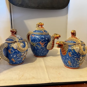May include: A blue and gold porcelain tea set with dragon handles and lids. The set includes a teapot, creamer, and sugar bowl.