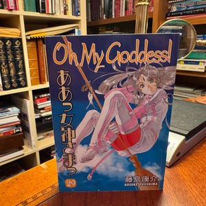 May include: A manga volume titled Oh My Goddess! volume 29 by Kosuke Fujishima. The cover features an anime-style character with long hair, wearing a white and pink outfit, riding a broomstick against a blue sky with white clouds.