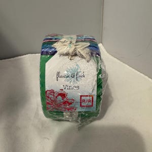 Peut inclure: Un rouleau de tissu avec un motif floral aux teintes vertes, bleues et violettes. Le tissu est étiqueté "Flaurie & Finch Vines" et "RJR Fabrics".