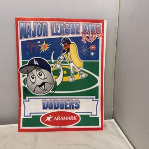 May include: A rectangular sign featuring the text "MAJOR LEAGUE KIDS" in blue and red. The sign has a baseball theme with a cartoon baseball wearing a Dodgers cap and a hot dog character swinging a bat. The word "DODGERS" is also displayed.