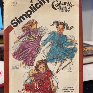May include: Simplicity sewing pattern number 5354 for a child's dress. The pattern includes three different styles: a purple dress with a lace collar, a blue dress with a lace collar, and a red dress with a floral print. The pattern is for a size 6 child.