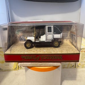 Könnte beinhalten: Ein Miniatur-Oldtimer-Modell in einer transparenten Vitrine. Das Auto ist weiß und schwarz mit goldfarbenen Rädern und Zierleisten. Die Vitrine hat einen roten Sockel mit der Aufschrift "MODELS OF YESTERYEAR". Das Auto ist mit "LONDON" beschriftet.