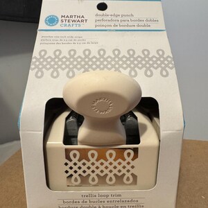May include: A cream-coloured Martha Stewart Crafts double-edge punch for trellis loop trim. The packaging features text in English and Spanish. The punch is designed to create 2.5 cm wide stripes.