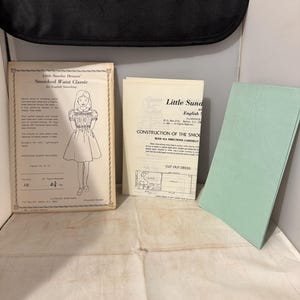 May include: A vintage sewing pattern for a smocked waist classic dress. The pattern includes instructions for English smocking and a cut-out dress pattern. The pattern is for sizes 10, 12, 14, and 16.