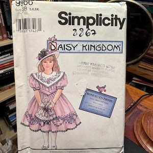 Può includere: Una busta per cartamodello Simplicity 9960 per un vestito Daisy Kingdom in taglia BB 5, 6, 6X. Il fronte mostra l'illustrazione di un bambino che indossa un vestito rosa con colletto floreale e cappello, mentre tiene in mano una bambola. Incluso un cartamodello per vestito da bambola.