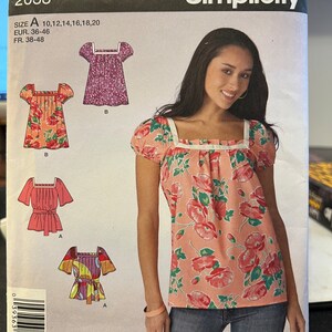 Puede incluir: Un patrón de costura para una blusa de mujer con escote cuadrado y mangas cortas. El patrón incluye tres vistas diferentes de la blusa, una con estampado floral, una con color sólido y una con estampado geométrico. El patrón es de Simplicity y es talla A, 10-20.