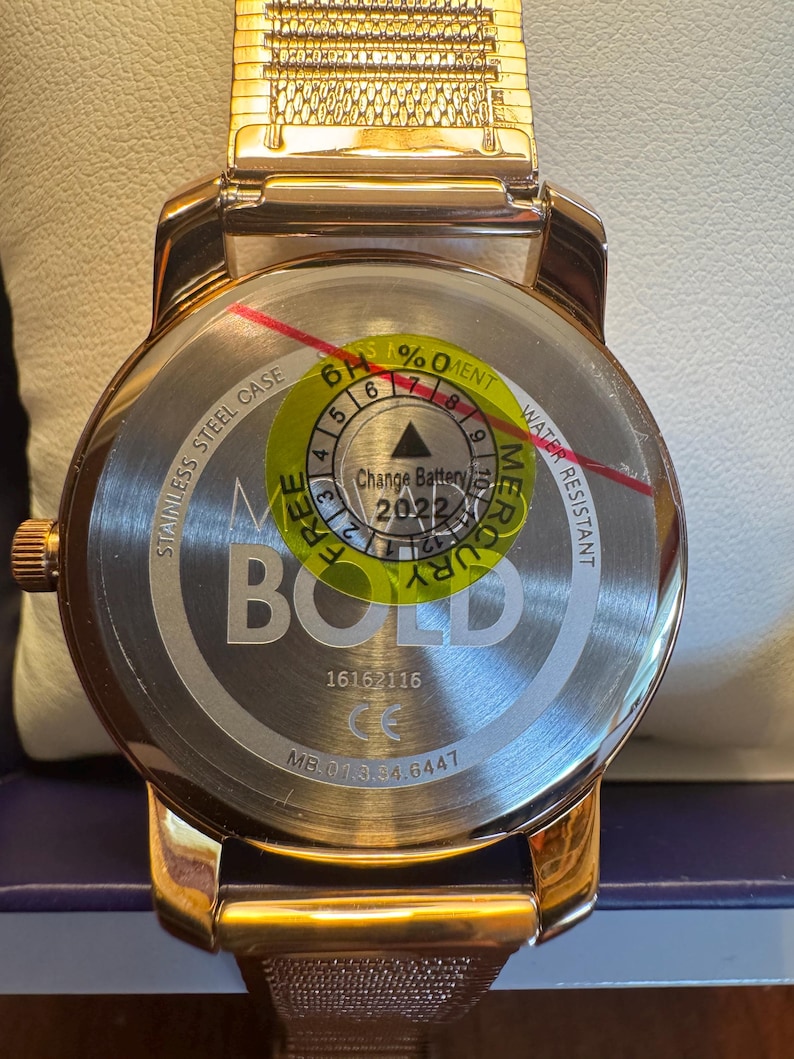 May include: A rose gold watch with a mesh band. The watch face is visible, with the text "BOLD" and "STAINLESS STEEL CASE". The back of the watch has a sticker indicating the battery change year is 2022.
