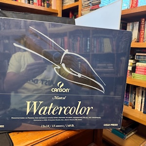 May include: A dark blue box of Canson Montval Watercolor paper. The box features a white paintbrush design and the words "Watercolor" and "Acid Free". The paper measures 12 x 16 inches and is cold press.