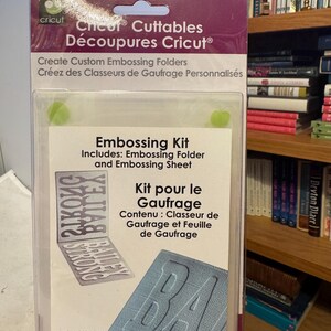 May include: A Cricut embossing kit in a clear plastic package. The kit includes an acrylic folder and embossing sheet. The package text reads "Create Custom Embossing Folders". The acrylic folder measures 4.25 inches by 5.75 inches.