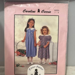 以下が含まれることがあります： ピンクの縫製パターン封筒に、ドレスを着た女の子2人の写真が載っています。パターンは「キャロライン＆キャリー」と呼ばれ、サイズは1〜8です。パターンはシェリー・マドックスによるもので、「ピター・パター」と呼ばれています。