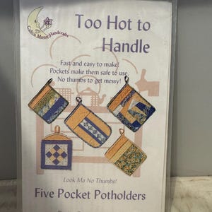May include: A craft pattern for five pocket potholders. The pattern is titled "Too Hot to Handle" and features a whimsical illustration of a moon with a flower. The text "Look Ma No Thumbs!" is also included. The pattern is for a quick and easy project, perfect for beginners.