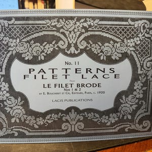 以下が含まれることがあります： 「Patterns Filet Lace」No. 11のヴィンテージ本の表紙。グレーの濃淡で表現された、複雑な花柄と幾何学模様が特徴です。タイトルが大きく表示され、出版社の名前と1920年という年号も確認できます。