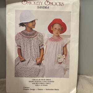 May include: A vintage sewing pattern for a girl's dress called "Sandra" by Smickety Smocks. The pattern includes instructions for a circular neck dress with short or long sleeves and a butterfly frill. The pattern is for sizes 5-8 years.