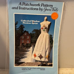 以下が含まれることがあります： 「大聖堂の窓 ホステスエプロン」のヴィンテージの裁縫パターン。パターンには、指示とエプロンを着た女性のカラーイラストが含まれています。エプロンは、ダイヤモンド柄の継ぎ合わせ生地で作られています。