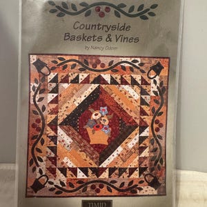 May include: A quilting pattern for a quilt titled "Countryside Baskets & Vines" by Nancy Odom. The pattern features a basket of flowers in the center surrounded by a vine border. The pattern is from Timid Thimble Creations.