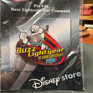 Op de afbeelding: Een Disney Store-speld met Buzz Lightyear uit Toy Story. De speld toont Buzz in zijn ruimtepak, met de tekst "Buzz Lightyear of Star Command 2000". De speld zit in een plastic verpakking.