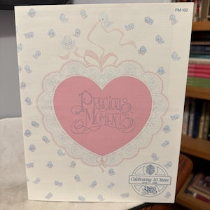 May include: A Precious Moments card with a pink heart design and the words "Precious Moments" in script. The card is decorated with small blue angel figures and a lace-like border. The card celebrates 10 years.