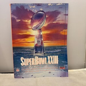 Può includere: Una copertina di rivista con il logo del Super Bowl XXIII e il trofeo Vince Lombardi. Lo sfondo mostra un tramonto sull'oceano. Il logo NFL è visibile.