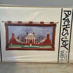 May include: A vintage craft pattern for a wall hanging featuring a colonial building with a red brick facade and a blue sky. The pattern is titled "Patches of Joy" and is from Williamsburg Colonial. The pattern is 84 cm by 43 cm.