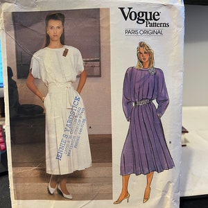 May include: Vogue Patterns Paris Original sewing pattern number 1553. The pattern features two dress designs. The first dress is white and the second dress is purple. The pattern is for a dress with a tie at the waist.
