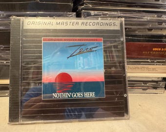 Può includere: Una custodia per CD con la scritta "ORIGINAL MASTER RECORDINGS". La copertina dell'album presenta un tramonto sull'acqua con la parola "Zero" e la frase "NOTHIN' GOES HERE". Il CD è in una custodia di plastica trasparente.