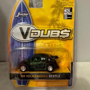 May include: A black 1:64 scale die-cast model of a 1959 Volkswagen Beetle with green flames and the words "No Spare Luck" on the side. The model is on a yellow background with the words "V DUBS" in white letters.