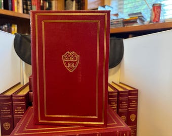 May include: A collection of hardcover books with red covers and gold accents. The front book displays a gold emblem. The books are part of "The Harvard Classics" series, suggesting a focus on classic literature and scholarly works.