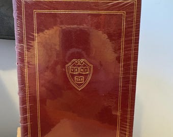 May include: A burgundy hardcover book with gold accents and a gold Harvard University seal on the front cover. The book is wrapped in plastic.