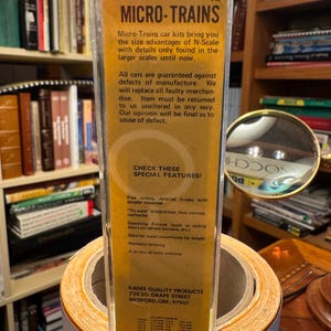 May include: A clear plastic package containing a Micro-Trains model train car kit. The packaging has a yellow and brown label with the brand name and product details. The text on the label highlights special features of the model train cars.