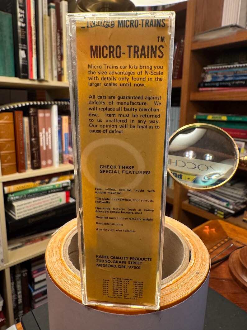 May include: A clear plastic package containing a Micro-Trains model train car kit. The packaging has a yellow and brown label with the brand name and product details. The text on the label highlights special features of the model train cars.