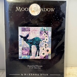 Może przedstawiać: Opakowanie z projektem bloku do pikowania. Projekt zawiera turkusową sylwetkę jelenia, białe kwiaty i patchworkowe tło. Tekst "Moon Shadow" znajduje się na górze, z "Fawn'd of Flowers" i "8" x 8" - Block Five" pod obrazem. Nazwisko projektanta to "by McKenna Ryan."