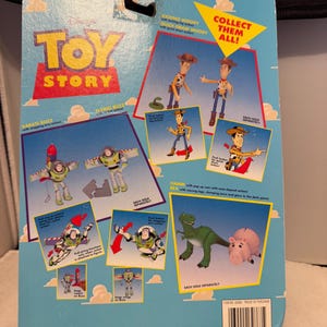 May include: A blue Toy Story action figure package featuring Woody, Buzz Lightyear, Hamm, and Rex. The package includes illustrations of the characters and the text "COLLECT THEM ALL!"