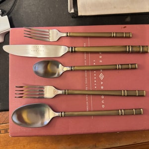 May include: A set of five gold-toned flatware pieces, including a knife, fork, and spoon, with the text "Joseph Abboud" and "Montana 18/10 Stainless Steel 5 Piece Place Setting" on the packaging.