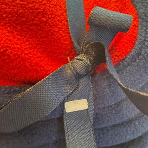 K&ouml;nnte beinhalten: Nahaufnahme einer gefalteten roten und marineblauen Fleece-Decke. Ein marineblaues Band ist mit einem Kunststoffclip um die Decke gebunden. Die Decke ist weich und flauschig, mit einer strukturierten Oberfl&auml;che.