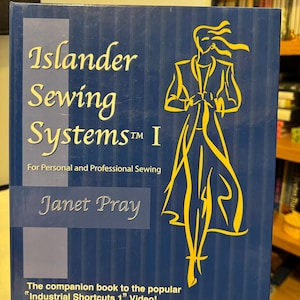 Può includere: Un libro blu intitolato "Islander Sewing Systems I" con lettere dorate e un'illustrazione gialla di una persona. Il libro è per il cucito personale e professionale ed è scritto da Janet Pray. Il libro è un complemento al video "Industrial Shortcuts 1".