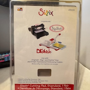 Może przedstawiać: Przezroczyste plastikowe opakowanie zawierające podkładki do cięcia Sizzix. Opakowanie zawiera logo Sizzix i informacje o produkcie, w tym kompatybilność z maszynami Big Shot i BIGkick. Tekst "Cutting Pad, Standard, 1 Pair" jest również zawarty.