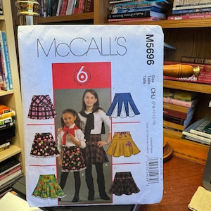 May include: McCall's M5696 sewing pattern featuring various skirt designs. The pattern includes illustrations of different skirt styles, with a focus on a plaid skirt and a floral skirt. The pattern size is CHJ (7-8-10-12-14).