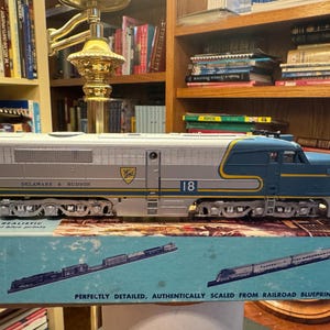 Puede incluir: Una locomotora de tren modelo plateada y azul, con las palabras "DELAWARE & HUDSON" y el número "18". El modelo está sobre una caja con la inscripción "PERFECTLY DETAILED, AUTHENTICALLY SCALED FROM RAILROAD BLUEPRINTS".