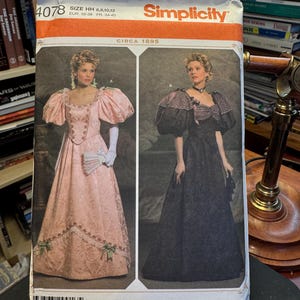 Könnte beinhalten: Simplicity Schnittmuster 4078, ca. 1895, mit zwei Frauen in eleganten Kleidern. Ein Kleid ist rosa mit Puffärmeln, das andere schwarz. Größen: 6, 8, 10 und 12, mit EUR-Größen 32-38 und FR 34-40.