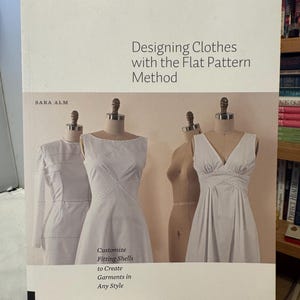 May include: A book titled "Designing Clothes with the Flat Pattern Method" by Sara Alm. The cover shows white dress forms displaying garment designs. The book's subtitle reads "Customize Fitting Shells to Create Garments in Any Style."