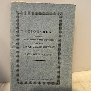 May include: A blue book with a black border and the title "RAGIONAMENTI" in black text. The text continues with "INTORNO AI DISPARERI E ALLE DISCORDIE CHE SONO TRA GLI ZELANTI CATTOLICI E I COSI DETTI INCREDULI". The book is signed "Guido Pimamontti" in blue ink.