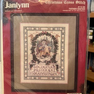 May include: A Janlynn cross-stitch kit with a Christmas theme, labelled "Father Winter." The finished size is 40.6 x 50.8 cm. The kit contains fabric, cotton floss, beads, a needle, and instructions. The design features an alphabet and a winter scene.