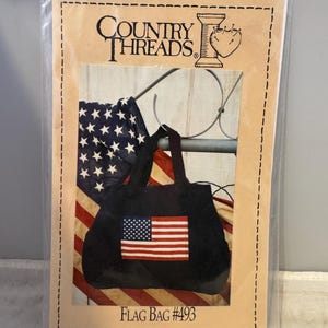 May include: A sewing pattern for a black tote bag with a red, white, and blue American flag design. The pattern is from Country Threads and is labeled "Flag Bag #493".