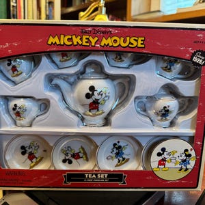 Könnte beinhalten: Eine verpackte Walt Disney's Mickey Mouse Tee-Set. Das Set enthält eine Teekanne, einen Sahnekännchen, eine Zuckerdose, Tassen und Untertassen. Jedes Stück ist weiß mit Mickey Mouse-Illustrationen. Die Box ist rot mit der Aufschrift "Mickey Mouse".