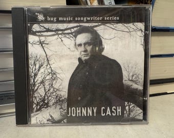 Puede incluir: Una caja de CD con una imagen en blanco y negro de Johnny Cash. La portada del álbum incluye el texto "bug music songwriter series" y "JOHNNY CASH" en fuente blanca. El fondo muestra una imagen en blanco y negro de un árbol.