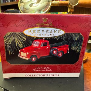 以下が含まれることがあります： 赤い箱に入った赤いHallmark Keepsakeオーナメント。オーナメントは、荷台にクリスマスツリーが載った1953年型GMCオールアメリカントラックです。「Keepsake Ornament」と「Collector's Series」の文字が箱に書かれています。