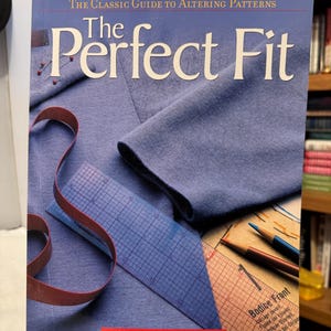 May include: A book titled "The Perfect Fit" with the subtitle "The Classic Guide to Altering Patterns." The cover shows blue fabric, pins, a measuring tape, and a ruler. The book contains 400 how-to photographs.