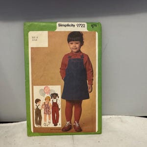 Könnte beinhalten: Simplicity 9722 Schnittmuster für ein Kinder-Latzkleid. Das Schnittmustercover zeigt ein junges Kind, das das Kleid trägt, mit einem roten Langarmshirt, einem marineblauen Latzkleid und roten Strumpfhosen. Das Cover zeigt auch Illustrationen von Kindern in verschiedenen Outfits.
